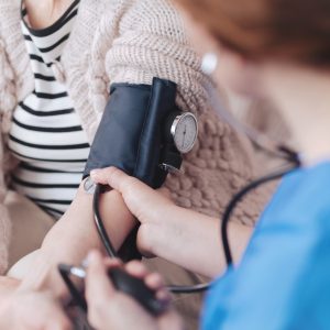 Κοντινή θέα σε μια γυναίκα νοσοκόμα που κάθεται μπροστά από έναν ηλικιωμένο ασθενή ενώ μετράει την αρτηριακή της πίεση κατά τη διάρκεια μιας τακτικής επίσκεψης. Κοντινή θέα σε μια γυναίκα νοσοκόμα που κάθεται μπροστά από έναν ηλικιωμένο ασθενή ενώ μετράει την αρτηριακή της πίεση κατά τη διάρκεια μιας τακτικής επίσκεψης.